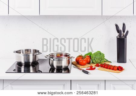 Ripe Vegetables On Kitchen Counter, Pans On Electric Stove In Light Kitchen