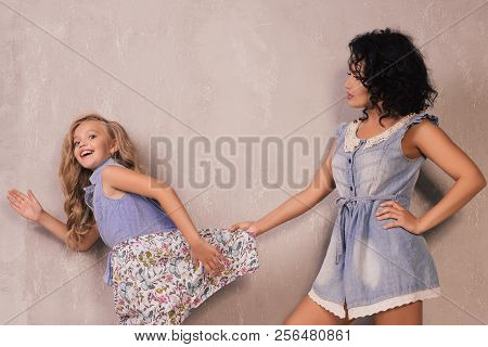 An Adult Mother Holds A Running Daughter For A Dress Near Grey Wall
