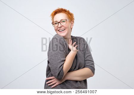 Pretty Caucasian Mature Woman With Short Red Hairstyle In Simple Pulover Is Shy To Hear A Compliment