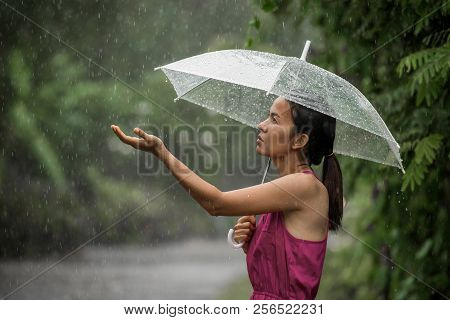 Beautiful Young Woman So Sad As She Holds Out Her Palm To Catch Falling Water. She Is Holding An Umb