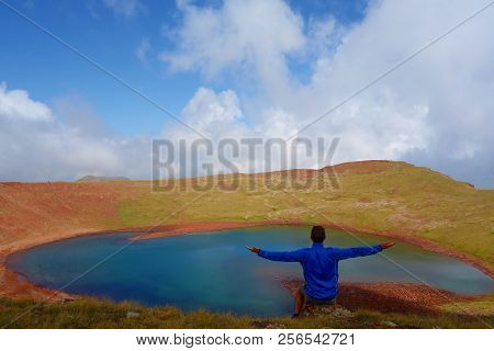 Young Man Sitting At The Edge Of Azhdahak Volcano With A Turquoise Lake Hidden Inside In Geghama Mou