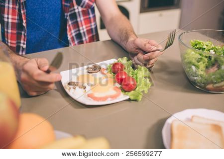 A Picture Of Tasty Omlet With Letuce And Cherry Tomatoes On Plate On Table. Guy Holds Knife And Fork