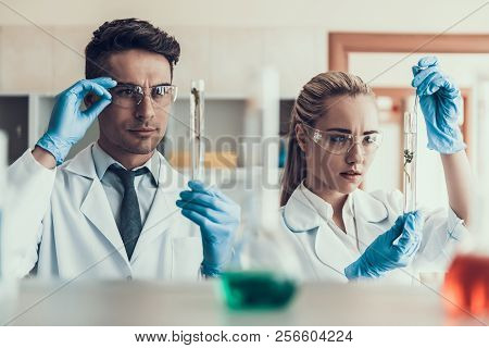 Young Scientists Look At Sampes In Laboratory. Researchers Wearing White Coats Gloves And Protective