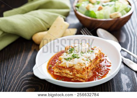 Traditional Lasagna On White Plate With Caesar Salad And Breadsticks