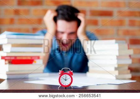 Young Man In Shirt With Books And Alarm Clock On Foreground.