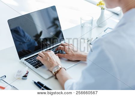 Partial View Of Female Doctor Typing On Laptop With Blank Screen At Table In Office