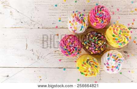 Colorful cup cakes on wooden background, top view.