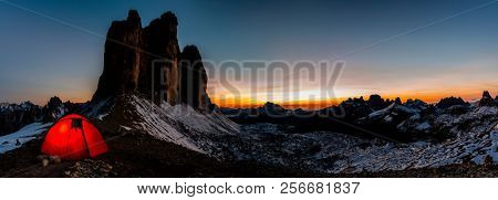 Night bivouac at Tre Cime di Lavaredo, milion star hotel under night sky, red illuminated tent on pass in Dolomites, Italy.