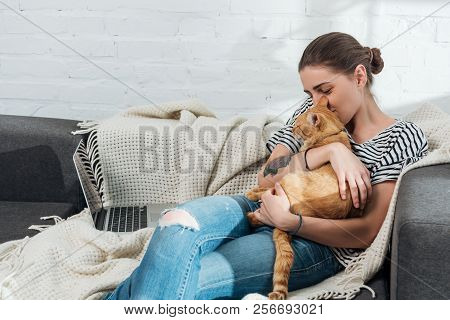 Happy Young Woman Holding Red Cat While Using Laptop At Home
