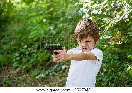 Little Kid Sniper Point Gun In Target Carefully Aiming Outdoors On Green Treees Background
