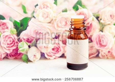 Glass Bottle Of Essential Oil With Empty Craft Label On Table With Roses Pink Soft Blurred Backgroun