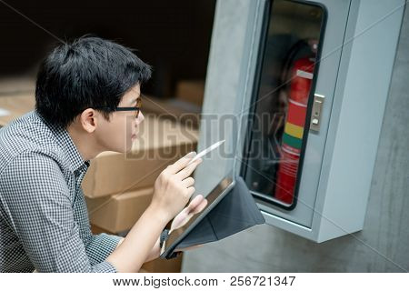 Young Asian Male Technician Checking Red Fire Extinguisher In Fire Hose Cabinet (fhc) By Using Digit
