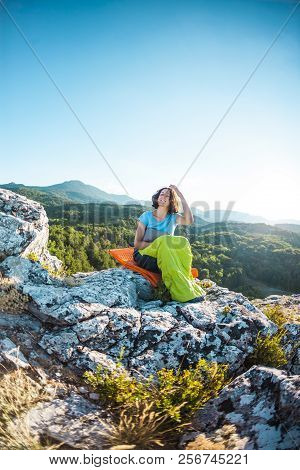 A Woman Is Sitting In A Sleeping Bag On Top Of A Mountain. A Smiling Girl Rests After A Climb. The B