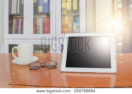 Mock Up Image Of White Tablet Pc With Black Blank Screen And Coffee Cup On Wooden Table In Blur Offi