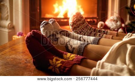 Young Family Wearing Warm Woolen Socks And Lying Under Blanket Relaxing At Fireplace