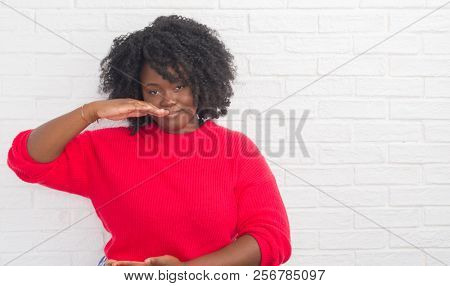 Young african american plus size woman over white brick wall gesturing with hands showing big and large size sign, measure symbol. Smiling looking at the camera. Measuring concept.
