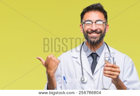 Adult hispanic doctor man drinking glass of water over isolated background pointing and showing with thumb up to the side with happy face smiling