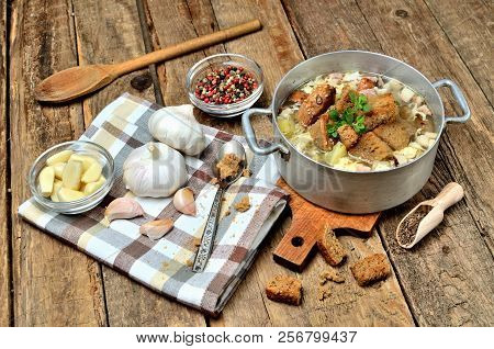 Garlic Soup In An Old Saucepan, Fresh Garlic Bulbs, Cloves, Colored Pepper, Wooden Spoon, Croutons A