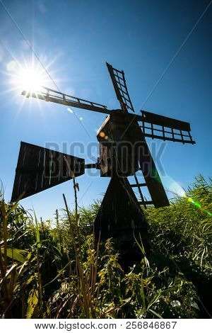 Characteristic Black Tarred Windmill Between Green Reeds At The Edge Of A Grassland And Waterways. U