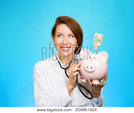 Closeup Portrait Of A Doctor Or Nurse Listening With Stethoscope To Piggy Bank With Dollar Bill