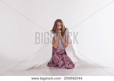 A Beautiful Girl With White Wings Is Kneeling With Her Hands Folded For Prayer. Guardian Angel In Pi