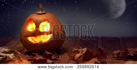 Jack o lanterns Halloween pumpkin face on wooden background and autumn leafs