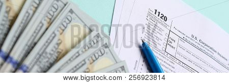 1120 Tax Form Lies Near Hundred Dollar Bills And Blue Pen On A Light Blue Background. Us Corporation