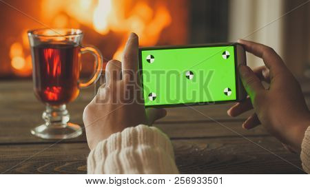 Closeup Image Of Woman Holding Smartphone And Making Photo Of Firepalce At House. Empty Green Screen