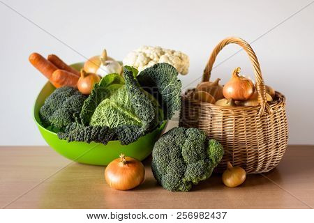 Organic Vegetables - Savoy Cabbage, Broccoli, Carrots, Garlic And Golden Onions In A Basket On The W