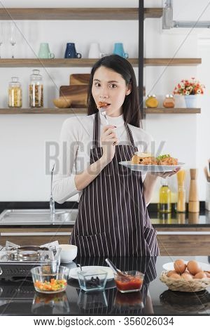 Asian Woman In Eating Fried Rice, There Are Stove And Ingredents On Counter, Concept For Cooking In 