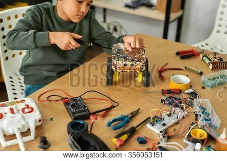 Close Up Of A Boy Using Screwdriver While Fixing Bolts On A Robot Vehicle. Smart Kids And Stem Educa