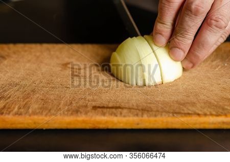 The Process Of Cutting Onions On A Cutting Board. A Male Hand Chopped Half A White Onion With A Knif