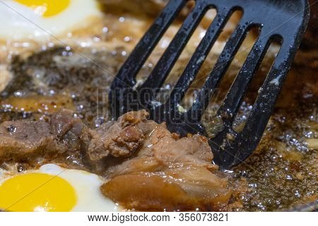 Fried Eggs, Black Spatula Turns Over Pieces Of Meat In A Pan In Sunflower Oil Close-up. The Concept 