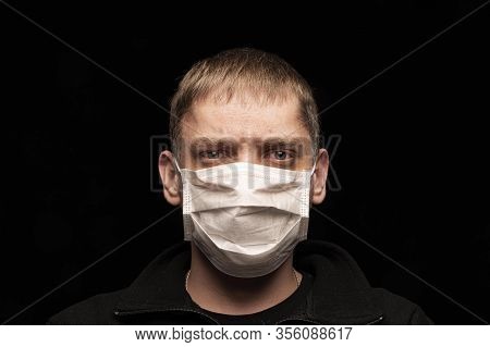 A Sick Male Patient In A Protective Medical Anti-bacterial Mask Looks Intently At The Camera, Afraid