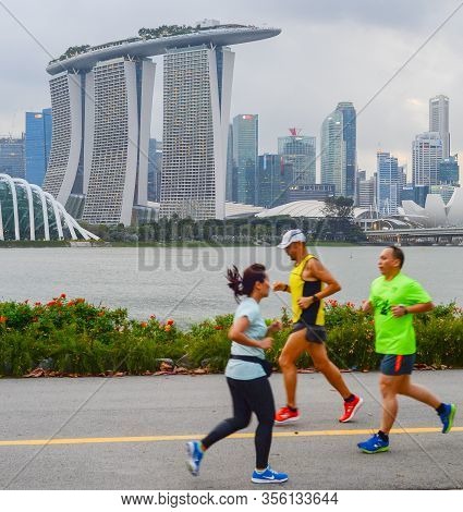 Singapore - February 16, 2017: People Running By The Embankment Of Singapore River In Front Of Singa