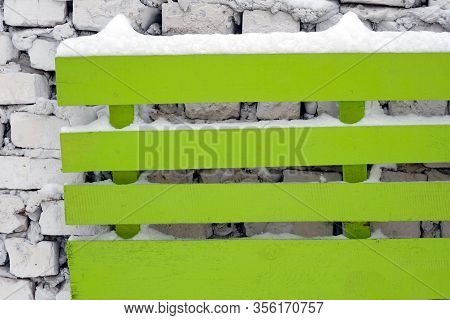 Green Wooden Boards Attached To A White Brick Wall. The Boards Are Covered With Snow And Hang On The