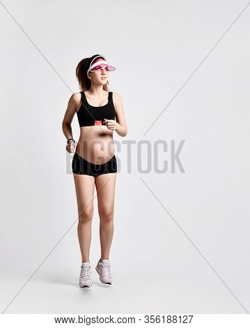 Pregnant Girl With Belly, In Green Sun Visor, Black Sport Shorts And Top, Pink Sneakers. She Is Jogg