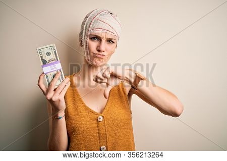 Young woman injured wearing bandage on head holding money from medical insurance payment with angry face, negative sign showing dislike with thumbs down, rejection concept