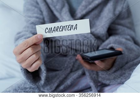 closeup of a man, wearing a gray robe staying at home or a hotel room, showing a note with the word cuarentena, quarantine in spanish written in it