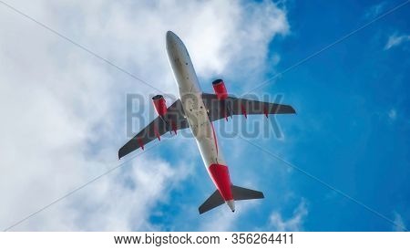 Underbelly Of A Jet Airplane Flying In The Air Isolated Against A Blue Sky With Clouds