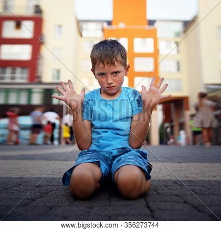 A Little Boy Sits On The Ground With His Hands Up And Protests. The Concept Of Raising A Difficult N