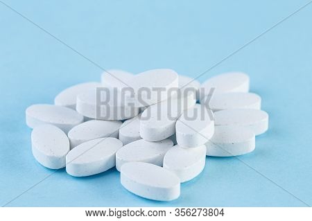 Heap Of White Medical Pills On A Light Blue Background. Pharmaceutical Medicament, Cure For Health. 