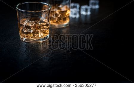 Whisky, Whiskey, Bourbon Or Cognac With Ice Cudes On Black Stone Table