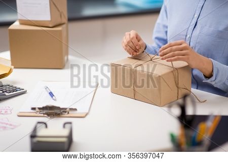 delivery, mail service, people and shipment concept - close up of woman packing parcel box and tying rope at post office