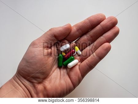 Male Hand Keeping Pills Of Diffetent Colors On White Background