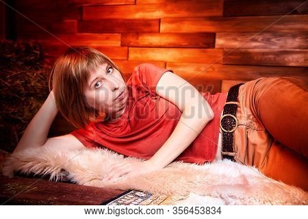 Ugly Pity Girl In Red Dress On The Couch With Hay In The Room Or In The Hayloft With Wooden Walls. R