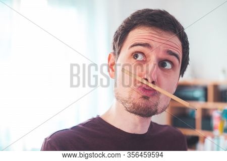 Fooling Around At Home. Bored Young Man With A Trapped Pencil Between Nose And Lips