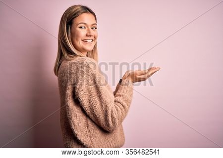 Young beautiful blonde woman wearing winter wool sweater over pink isolated background pointing aside with hands open palms showing copy space, presenting advertisement smiling excited happy