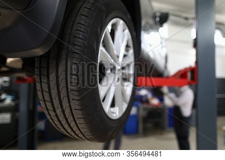 Close-up View Of Car All-season Tire With Aluminum Rim. Mechanical Lift For Vehicle. Automobile Serv
