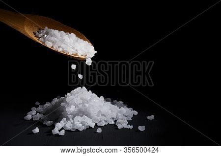 Sea Salt Crystals Fall From Spoon On A Pile Of Salt, Black Background